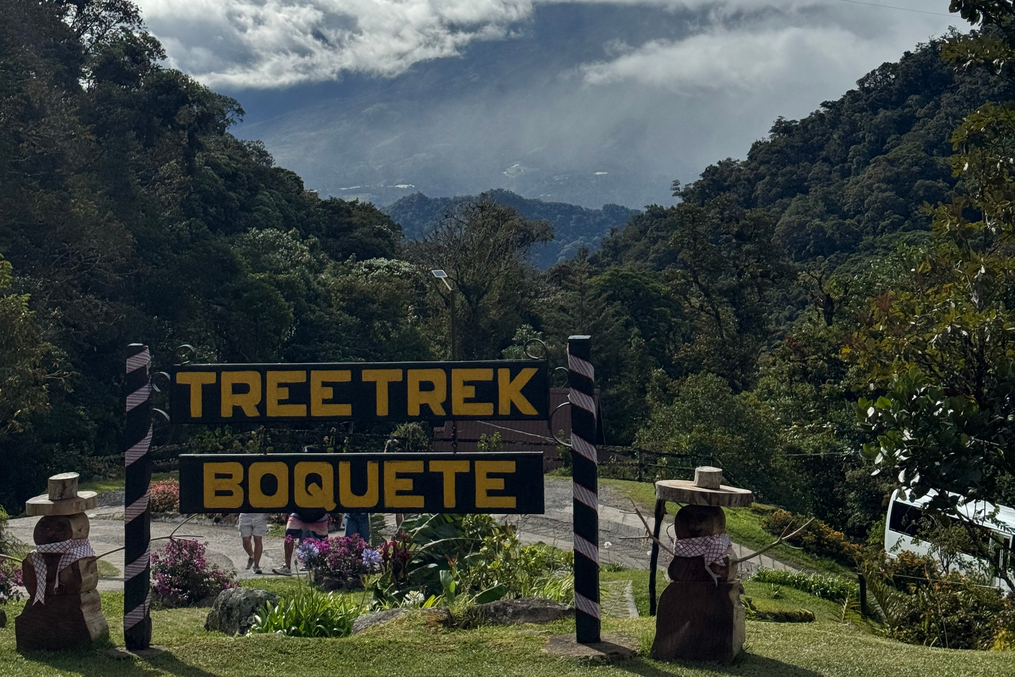 Scenic mountain view above the “Tree Trek Boquete” entrance sign, surrounded by lush forest and low clouds.